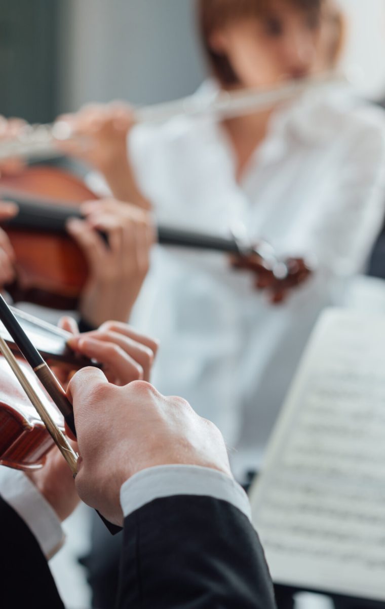 Confident violinist playing his instrument and reading a music sheet, classical music symphony orchestra performing on background